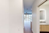 Located at 945 Mid City Drive in Huntsville, Alabama, this thoughtfully designed unit offers a clean, modern aesthetic across a single floor. The open-concept kitchen and living room serve as the heart of the space, where warm hardwood-style flooring and crisp white walls create a bright, welcoming atmosphere. The living area is anchored by floor-to-ceiling windows that span the exterior wall, flooding the space with natural light and offering views of the surrounding mid-city development. A ceiling fan adds both style and function overhead. The kitchen is well-appointed with light wood flat-front cabinetry, stainless steel appliances including a French door refrigerator, electric range, built-in microwave, and dishwasher. A tiled backsplash with a subtle mosaic pattern, light quartz countertops, a deep undermount sink with a matte black faucet, and open industrial-style shelving complete the culinary space. Pendant lighting adds a modern touch above the counters. The bathroom features a frameless glass walk-in shower, large-format tile flooring, and a wood-accented vanity with a stone countertop, maintaining the unit's clean, contemporary character. A dedicated closet provides practical storage. The overall design is cohesive and modern, ideal for efficient urban living.