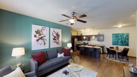 This single-floor residence offers a thoughtfully designed open-concept layout that seamlessly connects the living area to the kitchen. The living room features rich hardwood-style flooring, a ceiling fan with light fixture, and a teal accent wall that adds a bold pop of color. Large windows allow natural light to fill the space, while the entry door provides a clean transition into the home.

The kitchen is a standout feature, showcasing dark espresso cabinetry, granite countertops, and a full suite of stainless steel appliances including a refrigerator, range, microwave, and dishwasher. A built-in wine rack adds a sophisticated touch, and pendant lighting over the island enhances the space's modern aesthetic. The kitchen island doubles as a breakfast bar with seating.

The bedroom is a comfortable retreat with plush carpet, large windows dressed with curtain panels, and ample space for a full bedroom suite. The room connects to a walk-through closet that leads conveniently toward the kitchen area. Two full bathrooms feature granite vanity tops, dark cabinetry, tub-shower combinations, and hardwood-style flooring. An in-unit laundry area with a full-size washer and utility shelf rounds out this well-equipped residence.
