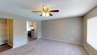 This single-floor residence offers a functional and comfortable layout designed for everyday living. The living room is generously proportioned, featuring soft carpeting, neutral gray-toned walls, a textured ceiling, and a ceiling fan with integrated lighting. A large window and sliding glass door allow natural light to fill the space, while a wall-mounted air conditioning unit provides climate control. The galley-style kitchen is well-appointed with gray cabinetry extending to the ceiling for ample storage, laminate wood-style flooring, a black gas range, a full-size refrigerator, a sink with a countertop peninsula, and a range hood. The kitchen opens toward a dining area with a ceiling fan and access to a sliding glass door with vertical blinds. Two bedrooms are carpeted and finished with the same warm neutral palette, each featuring a ceiling fan with light, textured ceilings, and windows with vertical blinds that provide natural light. The two bathrooms are clean and bright; one includes a shower/tub combination with chrome fixtures, while the second features a stand-up glass-enclosed shower, a vanity with a granite-style countertop, and wood-style flooring. Throughout, the space maintains a cohesive, understated aesthetic suited to a variety of lifestyles.