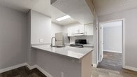 This single-floor unit offers a thoughtfully designed layout with a consistent, modern aesthetic carried throughout every room. The kitchen serves as a central highlight, featuring a peninsula with a stone-look countertop and an integrated sink — ideal for both meal prep and casual dining. White shaker-style cabinetry lines the walls, complemented by stainless steel appliances including a refrigerator and an electric range with a ventilation hood. Recessed panel lighting brightens the kitchen space efficiently.

Wood-look flooring runs throughout the unit, providing a warm, cohesive look that contrasts nicely with the neutral gray walls. The bedrooms are well-proportioned, with at least one room featuring a window fitted with horizontal blinds that allows natural light to filter in. Textured ceilings add a subtle layer of character to the interior.

The bathroom is clean and functional, featuring a full tub-shower combination, a toilet, and a vanity with a stone-look countertop, finished with chrome fixtures and wood-look flooring that mirrors the rest of the unit. White trim and baseboards frame each room neatly, contributing to the overall bright and tidy presentation of this move-in-ready space.