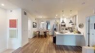 This thoughtfully designed single-floor residence offers a seamless blend of modern aesthetics and functional living. The open-concept layout connects the kitchen, dining, and living areas, creating a cohesive and inviting atmosphere throughout. Warm wood-look flooring flows consistently across the main living spaces, anchoring the bright, white-toned interior.

The kitchen is a standout feature, outfitted with crisp white shaker cabinetry, a quartz waterfall island with pendant lighting, stainless steel appliances including a French door refrigerator, electric range with a stainless hood, and a built-in microwave. Subway tile backsplash adds a clean, classic touch. The adjacent dining area comfortably seats six and is highlighted by a modern globe pendant light.

The living room offers a relaxed, open feel with a ceiling fan, sliding panel doors that invite natural light, and a wall-mounted television setup.

Both bedrooms are carpeted and generously proportioned, each featuring ceiling fans and ample natural light through plantation-shuttered windows. The primary bathroom impresses with a large backlit vanity mirror, quartz countertops, white cabinetry, and a glass-enclosed walk-in shower. The secondary bathroom mirrors this refined style with a quartz vanity and a shower-tub combination.