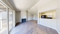 Located at 2167 NE Loop 410 in San Antonio, TX, this generously proportioned one-bedroom, one-bathroom residence offers a well-designed single-floor layout with a variety of notable architectural details. The living room is a standout space, boasting soaring vaulted ceilings, a classic wood-burning fireplace with a white mantel and tile surround, and rich hardwood-style flooring that extends throughout the main living areas. A sliding glass door floods the room with natural light and opens directly onto a private balcony enclosed by decorative iron railings, offering pleasant views of the landscaped courtyard below. The galley-style kitchen is efficiently arranged, featuring white cabinetry, light countertops, a double sink, and black appliances including a full-size refrigerator and dishwasher, all set on durable wood-look flooring. The bedroom is a comfortable retreat with plush carpeting, a ceiling fan with integrated lighting, and a window that allows natural light to brighten the room. The bathroom is clean and functional, finished with wood-look flooring and a full tub-shower combination. Neutral tones and clean lines throughout give this residence a bright, move-in-ready feel.