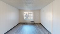 This efficiently designed single-floor unit offers a thoughtful layout across four distinct areas, making smart use of its compact footprint. The living area features wood-look luxury vinyl flooring, neutral-toned walls, and a textured ceiling, creating a clean and versatile space bathed in natural light from a front-facing window. A wall-mounted HVAC unit provides year-round climate control. The kitchen is well-appointed with bright white shaker-style cabinetry, gray countertops, a stainless steel sink, and a full suite of stainless steel appliances including a gas range, microwave, and oven. The open layout between the kitchen and living space enhances the sense of flow throughout. The bathroom is finished with durable wood-look vinyl flooring, a white vanity with granite-style countertops, and a clean white tub and shower combination illuminated by a high, narrow window that brings in natural light while maintaining privacy. Throughout the unit, a consistent palette of white walls and wood-tone flooring creates a cohesive and modern aesthetic, offering a move-in-ready space suited for comfortable everyday living.