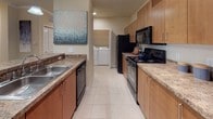 This single-floor residence offers a thoughtfully designed layout across several well-defined living spaces. The open-concept living area is finished with plush carpeting, crown molding, and a ceiling fan, while large windows with blinds allow natural light to fill the room. A door provides direct outdoor access, enhancing the sense of openness. The living space flows seamlessly into the kitchen, which features granite-style countertops, warm wood cabinetry, tile flooring, black appliances, and pendant lighting over a breakfast bar. A dedicated in-unit laundry room with a full-size washer and dryer is conveniently accessible from the kitchen.

The primary bedroom is generously sized with plush carpet, a ceiling fan, a walk-in closet, and direct access to a private en-suite bathroom. The en-suite features an expansive L-shaped vanity with dual sinks, warm wood cabinetry, and tile flooring. A second bedroom, also carpeted with a ceiling fan and natural light from a window, is served by a second full bathroom with tile flooring, a single vanity, and a tub-shower combination. Throughout, the neutral warm tones and consistent finishes create a cohesive and comfortable ambiance.