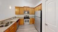 Located at 4825 Walburg Landing St in Winston Salem, North Carolina, this single-floor home offers a well-organized layout with a clean, neutral aesthetic throughout. The kitchen is thoughtfully appointed with warm honey-toned cabinetry, granite countertops, and a full suite of stainless steel appliances, including a refrigerator, range, and over-the-range microwave. Light hardwood-style flooring runs through the kitchen and adjoining dining area, which is illuminated by an elegant pendant chandelier. The dining space flows naturally from the kitchen, creating a cohesive and functional living environment. The bedrooms are finished with plush carpeting and crisp white walls, offering a comfortable and versatile space. One bedroom features a ceiling fan with a light fixture and a window with outdoor views of the surrounding greenery. The primary bedroom benefits from a vaulted ceiling detail, adding a sense of openness and volume to the space. The bathroom is well-appointed with granite countertops on warm wood vanity cabinetry, a soaking tub and shower combination with chrome fixtures, wood-look flooring, and a window providing natural light. Throughout the home, arched doorways, white panel doors, and clean white baseboards add architectural character and a polished, cohesive finish.