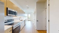 Located at 405 40th Ave N in Nashville, TN, this modern single-floor studio presents a thoughtfully designed open-concept layout that combines the kitchen and living area into one cohesive space. Light oak-toned luxury vinyl plank flooring runs throughout, lending warmth and continuity to the interior.

The kitchen is outfitted with flat-front light wood cabinetry, under-cabinet lighting, a subway tile backsplash, white quartz countertops, and stainless steel appliances including a refrigerator, oven, and built-in microwave. The open living area benefits from large floor-to-ceiling windows and a glass sliding door that leads to a private balcony, filling the space with abundant natural light and offering views of the surrounding Nashville neighborhood. A ceiling fan adds practical comfort to the living area.

The bathroom features a light wood vanity with a white countertop, recessed lighting, large-format tile flooring, and a walk-in shower with white tile surround. A dedicated closet provides convenient storage. The unit's clean white walls, modern black hardware accents, and minimalist aesthetic create a bright, contemporary ambiance well suited to urban living in Nashville's growing 40th Avenue North corridor.