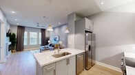 Located at 1812 Hickory Street in Dallas, TX, this modern 1-bedroom, 2-bathroom residence offers a well-designed single-floor layout with contemporary finishes throughout. Light hardwood flooring flows seamlessly across the open-concept living and kitchen areas, creating a cohesive and inviting atmosphere.

The living room is bright and comfortable, featuring recessed lighting, a ceiling fan, a wall-mounted electric fireplace, and large windows dressed with elegant drapes that invite natural light. The kitchen is a standout, boasting sleek gray flat-front cabinetry, quartz countertops with a distinctive veining pattern, stainless steel appliances, and a peninsula with seating for two — all illuminated by stylish pendant lights.

The spacious primary bedroom offers a serene retreat with a ceiling fan, natural light from a window with blinds, and direct access to a dedicated en-suite bathroom. The en-suite features large-format tile flooring, a glass-enclosed walk-in shower with hexagonal tile surround, and a modern vanity. A well-organized walk-in closet with multi-tier rods and open shelving provides generous storage. A second full bathroom serves as a guest bath. The overall palette of soft grays and whites contributes to a clean, contemporary aesthetic throughout.