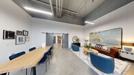 Located at 4015 133rd St SE in Mill Creek, WA, this single-floor loft-style unit offers a striking industrial-modern aesthetic defined by soaring ceilings with exposed ductwork, polished concrete floors, and an abundance of natural light streaming through large black-framed glass doors and transom windows. The open main area seamlessly integrates a dining space and living room, where a sliding barn door adds a functional yet stylish architectural detail. The living area features a cozy seating arrangement anchored by a textured area rug, complemented by warm and eclectic décor. The kitchen is thoughtfully designed with wood-toned cabinetry, open shelving, a tile backsplash, quartz countertops, and stainless steel appliances including a range, refrigerator, and range hood. The bathroom offers a bold, spa-like atmosphere with deep navy accent walls, a shower, and open wood shelving for storage. A dedicated laundry area houses a full-size front-loading washer and dryer. Linear pendant lighting and clean white walls throughout enhance the bright, contemporary feel of this well-appointed space.