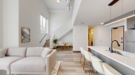 Located at 2132 Stokes Blvd in Cleveland's vibrant University Circle neighborhood, this modern two-story home offers a thoughtfully designed layout across two floors. The main level makes a striking first impression with soaring double-height ceilings in the living area, flooding the space with natural light through oversized windows that frame views of the surrounding neighborhood. Light wood-tone flooring flows seamlessly throughout, complementing the crisp white walls and creating a bright, airy ambiance. The open-concept layout connects the living, dining, and kitchen areas into one cohesive space, ideal for both everyday living and entertaining. The kitchen is outfitted with sleek gray cabinetry, stainless steel appliances, and a large island with bar seating accented by gold-legged white chairs beneath a modern pendant light. A convenient half bath is also found on the main level. A staircase leads to the upper floor, where the private bedroom retreat offers a serene atmosphere with warm wood furnishings and a dedicated closet. Two full bathrooms feature clean, contemporary finishes with gray vanities and matte black hardware. A dedicated laundry closet with a stacked washer and dryer adds everyday convenience, completing this well-appointed urban home.