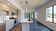 Located at 5211 Peachtree Blvd in Chamblee, Georgia, this contemporary single-floor residence showcases a clean, modern design throughout. The open-concept living and kitchen area is a standout feature, anchored by a sleek center island with a crisp white countertop, ideal for dining or meal preparation. The kitchen is outfitted with stainless steel appliances, including a French door refrigerator, gas range, microwave, and dishwasher, all complemented by light wood cabinetry that extends floor to ceiling for generous storage. Dark hardwood flooring runs throughout the living spaces, providing a rich contrast to the bright white walls and ceilings. Large windows and a full-width glass sliding door flood the main living area with natural light and open to a private balcony with outdoor views. The bedrooms are well-proportioned with hardwood floors, ceiling fans, and windows that frame green surroundings. The primary bathroom features a dual-sink vanity with light wood cabinetry, white countertops, a large mirror, and a glass-enclosed shower, all finished with large-format tile flooring. A well-organized walk-in closet with built-in shelving and drawer units completes the primary suite. A secondary bathroom offers a clean, minimalist design with an undermount sink and modern fixtures.
