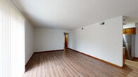 This single-floor unit offers a practical and comfortable layout designed for everyday living. The spacious living area is finished with durable wood-look laminate flooring and warm wood baseboards, creating a clean, cohesive aesthetic throughout the main spaces. A sliding glass door floods the room with natural light and provides direct outdoor access. The open layout connects the living area seamlessly to the galley-style kitchen, which is well-equipped with warm-toned oak cabinetry, granite-look countertops, and stainless steel appliances including a refrigerator, electric range, microwave, and dishwasher. Light wood-look flooring continues through the kitchen, enhancing the bright and functional workspace. A dedicated utility area off the kitchen includes a water heater and washer/dryer hookups, adding convenience. The two bedrooms are carpeted in neutral tones and feature natural light through blinds-equipped windows, with warm wood trim throughout. One bedroom includes access to a walk-in closet area. The full bathroom presents a clean, all-white finish with a tub-shower combination, modern fixtures, and a single vanity with storage. Textured ceilings and consistent trim details tie the space together with a cohesive, well-maintained character.