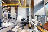 Located at 2408 South Blvd in Charlotte, NC, this contemporary fitness center delivers a well-appointed workout environment across a single, generously sized floor. The space is divided into two functional zones designed to accommodate a wide range of training needs.

The strength training area is anchored by a white multi-station power rack equipped with TRX suspension systems, accompanied by adjustable benches, a full dumbbell rack, kettlebells, medicine balls, and plate-loaded equipment. A wall of mirrors enhances the sense of depth and allows users to monitor their form throughout their workout.

The cardio zone features an array of modern machines, including treadmills, ellipticals, stair climbers, and rowers, all bathed in abundant natural light streaming through large floor-to-ceiling windows. Soaring ceilings with exposed gold-finish ductwork give the space an industrial-chic aesthetic, while recessed and pendant lighting ensures excellent visibility throughout.

A standout design element is the dramatic tiger mural that spans an entire wall, adding a bold, artistic focal point that energizes the space. The floors are finished in a distinctive scalloped pattern in neutral tones, tying the vibrant design together. The overall ambiance is energetic yet refined, making this fitness center a compelling and functional amenity.