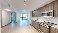 Located in Miami's vibrant Upper East Side neighborhood, this modern one-bedroom, one-bathroom residence offers a thoughtfully designed open-concept layout with clean lines and contemporary finishes throughout. Light-toned porcelain tile flooring runs seamlessly across the entire unit, enhancing the bright, airy atmosphere.

The combined kitchen and living area serves as the heart of the home. The kitchen is outfitted with rich wood-grain cabinetry, stainless steel appliances including a built-in microwave, dishwasher, and range, complemented by white quartz countertops and a marble-style backsplash. Floor-to-ceiling sliding glass doors flood the living area with natural light and open directly onto a private balcony, where tropical palm trees and lush landscaping create a serene outdoor setting.

The bedroom is a well-proportioned, tranquil space with neutral white walls and tile flooring, accompanied by a dedicated walk-in closet featuring built-in shelving and hanging rods. The bathroom is finished in a clean, modern style with a floating wood-grain vanity, white quartz countertop, undermount sink, and a large wall mirror with overhead lighting. The entry foyer provides a practical transition space with access to an additional louvered utility closet.