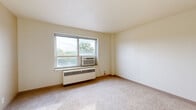 Located at 804 Cass St in La Crosse, Wisconsin, this 2-bedroom unit offers a practical and efficient single-floor layout. The space includes two bedrooms, a kitchen, a full bathroom, a closet, and a connecting hallway, making smart use of every square foot.

The primary bedroom is the most generously sized room, featuring wall-to-wall carpeting, a large window with an integrated air conditioning unit, and a baseboard heating system — providing year-round climate comfort. Views of surrounding trees are visible through the window, adding a touch of nature. A second bedroom mirrors a similar layout with carpeted flooring, a window with a window AC unit, and baseboard heating.

The kitchen is efficiently designed with warm wood cabinetry — both upper and lower — featuring frosted glass upper cabinet doors. Laminate countertops, a stainless steel sink, and a white electric range complete the functional cooking space.

The bathroom is finished with classic white wall tile accented by dark border tile, a tiled tub/shower combination, a woven-pattern tile floor, and chrome fixtures including a grab bar and towel bar.

A carpeted hallway connects the rooms, with light neutral-toned walls consistent throughout the unit, creating a clean and cohesive aesthetic.