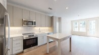 Located on North Arthur Ashe Boulevard in Richmond, Virginia, this two-bedroom, two-bathroom residence offers a thoughtfully designed single-level floor plan with a clean, contemporary aesthetic throughout. Light wood-tone flooring runs continuously through the main living areas, complementing the neutral color palette that gives the space a bright and airy feel.

The open-concept kitchen and living area serves as the heart of the home. The kitchen is outfitted with gray flat-front cabinetry extending to the ceiling for ample storage, stainless steel appliances including a refrigerator, range, and over-the-range microwave, a white subway tile backsplash with under-cabinet lighting, and a white countertop island ideal for dining or prep work. Large windows in the living area invite generous natural light and offer views of the surrounding community.

The spacious primary bedroom features a walk-in closet and a private en suite bathroom with a glass-enclosed shower, gray vanity cabinetry, and tile flooring. The second bedroom is well-sized with a dedicated closet and bright windows. The second bathroom includes a full soaking tub with tile surround. Additional highlights include multiple closets throughout, a dedicated laundry area, and a built-in desk nook for a functional workspace.