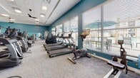 Located at 719 Lantern Walk Dr in Little River, SC, this single-floor fitness center is thoughtfully designed to support a full range of exercise routines. The space is divided into distinct workout zones, each outfitted with professional-grade equipment. The main cardio and strength area features bold teal accent walls, plush carpet flooring, and a drop tile ceiling with multiple ceiling fans that maintain airflow throughout. Rows of TRUE-brand treadmills, ellipticals, and stationary bikes line the perimeter, complemented by a comprehensive selection of selectorized strength machines and free weight stations. Large windows along one wall allow generous natural light to fill the room, offering views of the surrounding community. Mirrored wall sections enhance the sense of openness and allow users to monitor their form during training. A separate spin and group fitness studio features light hardwood flooring, wall-to-wall mirrors, sconce lighting, and multiple spin bikes alongside stability balls and other group fitness accessories. The open layout and distinct zones create an organized, functional environment. Throughout, the consistent teal color palette and clean, modern finishes give the facility a cohesive, energetic ambiance well-suited for daily fitness activities.