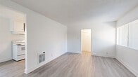 Located at 16131 Cornuta Avenue in Bellflower, CA, this efficiently designed one-bedroom, one-bathroom unit offers a well-organized single-floor layout comprising a living room, kitchen, bedroom, bathroom, and hallway. The living room is bright and open, featuring light gray wood-style laminate flooring, crisp white walls, a textured ceiling, and a wall-mounted heating unit. Natural light filters in through window blinds, enhancing the clean, airy atmosphere. A white entry door with a classic knob adds a simple, welcoming touch.

The galley-style kitchen is thoughtfully appointed with white cabinetry, granite-look countertops, a double-basin sink, a white electric range with overhead hood, and a full-size refrigerator. A window above the range area allows natural light into the cooking space, complementing the matching laminate flooring that flows throughout the common areas.

The bedroom offers a comfortable and quiet retreat, finished with plush neutral carpet, white walls, a window with blinds, and a flush-mount ceiling light fixture. The bathroom is clean and functional, featuring a full soaking tub with a tiled surround in a neutral stone pattern, a wall-mounted showerhead, a white vanity with a sink, and a mirror.