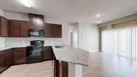 This 2-bedroom, 1-bathroom unit at Sage in Pueblo, Colorado offers a well-designed, single-story layout with a clean, modern aesthetic. The open-concept kitchen is a standout feature, showcasing rich dark-wood cabinetry, granite countertops, black appliances including a refrigerator, range, and built-in microwave, and a large peninsula with an integrated sink — ideal for both meal prep and casual dining. The kitchen flows seamlessly into the living area, which is bright and open with wood-style laminate flooring, neutral-toned walls, and a sliding glass door fitted with vertical blinds that allows for abundant natural light. Both bedrooms are comfortably sized, each featuring ceiling fans, windows with blinds, and the same warm wood-style flooring. The primary bedroom benefits from a generously sized walk-in closet with wire shelving for ample storage. The bathroom is equipped with a full tub-shower combination, white tile surround accented with a dark border, and overhead cabinetry. Wood-style flooring continues into the bathroom. A dedicated hallway and entrance area complete the functional floor plan, making this a well-organized and comfortable living space.
