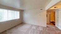 This single-story, one-bedroom, one-bathroom unit is designed with functionality and simplicity in mind. The layout makes efficient use of its footprint, providing comfortable living spaces throughout.

The living area features neutral-toned carpet flooring and smooth, light-colored walls that create a clean, open atmosphere. A large window fitted with vertical blinds allows natural light to fill the room, contributing to a bright and welcoming ambiance. Ceiling-mounted vents ensure consistent climate control throughout the space.

The bedroom continues the carpeted flooring and neutral color palette, offering a calm and restful environment. A window with blinds provides natural light and outdoor views. The room includes a built-in closet with louvered bifold doors, offering organized storage with an interior rod and shelving.

The bathroom is straightforward and practical, featuring a full-size soaking tub with a tiled surround and a shower curtain rod. A white vanity with a single-basin sink, a dark-framed mirror, and wall-mounted lighting complete the space. Neutral gray walls and tile flooring give the bathroom a clean, utilitarian feel.

Overall, the unit presents a simple, well-maintained living environment suited for everyday comfort.