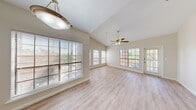 This single-floor residence offers a thoughtfully designed layout encompassing two bedrooms, two bathrooms, a living room, kitchen, hallway, and two closets. The spacious living room is a standout feature, boasting soaring vaulted ceilings, a ceiling fan with light fixture, and multiple large windows fitted with blinds that flood the space with natural light and offer views of surrounding greenery. Light wood laminate flooring runs consistently throughout, lending the home a clean, cohesive aesthetic. A separate dining area with a pendant light and wide windows provides an airy setting for meals. The kitchen is well-equipped with white cabinetry, granite countertops, stainless steel appliances including a range and dishwasher, and a pass-through that connects to the living area. The primary bedroom is generously sized, featuring vaulted ceilings, a ceiling fan, and access to a covered balcony through large windows. Both bathrooms are finished with granite vanity countertops, white cabinetry, and wood-look flooring. The closets include wire shelving systems for organized storage. Neutral wall tones throughout complement the bright, open feel of the home, creating a welcoming and functional living environment.