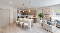 Located at Azalea Park in Naples, FL, this 1-bedroom, 1-bathroom unit offers a thoughtfully designed open-concept floor plan that maximizes its efficient footprint. Light wood-tone flooring runs throughout, complementing a bright, neutral color palette that enhances the sense of openness.

The kitchen is a standout feature, showcasing wood-grain cabinetry, a full suite of stainless steel appliances including a refrigerator with ice maker, range, microwave, and dishwasher, as well as a generous peninsula with a quartz countertop and bar seating for three — ideal for casual dining. Pendant lighting overhead adds a modern, polished touch. The kitchen flows seamlessly into the living area, which opens to a private balcony through sliding glass doors framed by floor-to-ceiling curtains, allowing abundant natural light.

The bedroom features soft blue-gray walls, a large window with natural light, and a ceiling fan. A dedicated closet provides ample storage. The bathroom is finished with tile flooring, a wood-toned vanity, and a glass-enclosed walk-in shower with full-height tile surround.

Rounding out the unit is a dedicated laundry room with full-size washer and dryer and overhead shelving, offering a practical convenience rarely found at this scale.