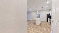 This well-designed single-story home offers three bedrooms, two bathrooms, and a thoughtfully laid-out floor plan that maximizes functionality and comfort. The open-concept kitchen and living area serves as the heart of the home, featuring crisp white shaker cabinets, a subway tile backsplash, stainless steel appliances — including a refrigerator, range, and over-the-range microwave — and a central island with a sink and light countertops. Stylish pendant lighting hangs above the island, complementing the recessed lighting throughout. Light-toned hardwood-style flooring flows seamlessly across all rooms, lending a bright, cohesive feel to the entire space. The living area extends to an exterior door with a glass panel, offering natural light and outdoor access. The generously sized primary bedroom connects to a well-appointed en-suite bathroom featuring a dual-sink vanity with white cabinetry, brushed nickel hardware, and large mirrors. Additional bedrooms are comfortable and naturally lit, each equipped with ceiling fans. A dedicated laundry room houses a full-size washer and dryer. The home also includes a spacious walk-in closet with wire shelving, providing ample storage. Neutral wall tones and clean finishes throughout create a modern, move-in-ready atmosphere.