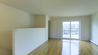 This single-floor space offers a clean, functional layout with a bright and open feel throughout. The main living area is finished with gleaming hardwood floors that reflect natural light, contributing to an airy and welcoming atmosphere. Neutral beige-toned walls provide a versatile backdrop suited to a variety of interior styles.

A standout feature of the living area is the large sliding glass door, which floods the space with natural light and provides direct access to an outdoor area. Views through the glass door reveal a green, landscaped exterior, enhancing the sense of connectivity with the outdoors.

A half-wall partition subtly defines the space, adding architectural character while maintaining an open flow between areas. A classic six-panel interior door provides access to an adjoining room, contributing to the space's practical layout. The smooth, white ceilings complement the light color palette and keep the interior feeling fresh and uncluttered.

Overall, this space combines functional design with an abundance of natural light, hardwood flooring, and a neutral aesthetic that creates a comfortable and adaptable living environment.