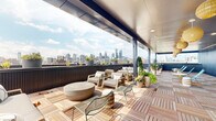 This rooftop amenity space seamlessly blends an indoor lounge with a generous open-air terrace, offering panoramic views of a prominent city skyline. The outdoor terrace is finished with interlocking wood deck tiles and partially covered by a sleek overhead canopy, providing both shade and shelter. Comfortable lounge seating, a round concrete coffee table, and an assortment of potted greenery create a well-appointed al fresco environment suited for socializing or unwinding.

The interior lounge makes a bold design statement with a full-wall botanical-print wallpaper featuring lush tropical foliage and florals. Emerald green velvet sofas, rattan accent tables, hanging planters, and eclectic decorative stools contribute to a vibrant, nature-inspired ambiance. Light wood-look flooring runs throughout, complementing the airy, bright atmosphere created by large windows and glass doors that frame city views and flood the space with natural light.

Adjacent to the lounge is a well-equipped kitchenette featuring light wood cabinetry, white quartz countertops, a stainless steel sink and refrigerator, and a distinctive pale blue vertical glass tile backsplash. Floor-to-ceiling glass doors open directly onto the terrace, creating a fluid indoor-outdoor connection ideal for entertaining.