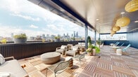 This rooftop amenity space seamlessly blends an indoor lounge with a generous open-air terrace, offering panoramic views of a prominent city skyline. The outdoor terrace is finished with interlocking wood deck tiles and partially covered by a sleek overhead canopy, providing both shade and shelter. Comfortable lounge seating, a round concrete coffee table, and an assortment of potted greenery create a well-appointed al fresco environment suited for socializing or unwinding.

The interior lounge makes a bold design statement with a full-wall botanical-print wallpaper featuring lush tropical foliage and florals. Emerald green velvet sofas, rattan accent tables, hanging planters, and eclectic decorative stools contribute to a vibrant, nature-inspired ambiance. Light wood-look flooring runs throughout, complementing the airy, bright atmosphere created by large windows and glass doors that frame city views and flood the space with natural light.

Adjacent to the lounge is a well-equipped kitchenette featuring light wood cabinetry, white quartz countertops, a stainless steel sink and refrigerator, and a distinctive pale blue vertical glass tile backsplash. Floor-to-ceiling glass doors open directly onto the terrace, creating a fluid indoor-outdoor connection ideal for entertaining.
