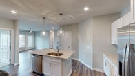 Located at 6029 W Gate City Blvd in Greensboro, NC, this single-floor residence offers a thoughtfully designed open-concept layout with contemporary finishes throughout. The kitchen serves as the centerpiece of the living area, showcasing white shaker-style cabinetry, granite countertops, and a large central island with an undermount sink. Stainless steel appliances, a subway tile backsplash in a soft blue-green hue, and dual pendant lights with glass shades contribute to the kitchen's polished, modern aesthetic. Rich-toned hardwood-style flooring runs through the main living and kitchen areas, complementing the neutral gray walls.

The bedrooms are carpeted for comfort, each equipped with ceiling fans and windows fitted with blinds that allow ample natural light. One bedroom features a built-in wall shelf, adding a functional architectural detail. The primary bathroom is generously proportioned, offering a dual-sink vanity with granite countertops, tile flooring, and direct access to a walk-in closet with built-in shelving. A secondary bathroom provides a single-sink vanity with matching finishes and tile flooring. Overall, the space presents a clean, cohesive design with modern fixtures and a bright, neutral palette throughout.