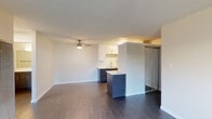 This single-floor unit offers a thoughtfully designed layout with a clean, modern aesthetic throughout. The open living area is anchored by dark hardwood-style flooring and features a ceiling fan, creating a comfortable and airy atmosphere. A dedicated closet with built-in white cabinetry provides generous storage. The kitchen is a standout feature, showcasing a two-tone design with sleek white upper cabinets and dark wood-textured lower cabinetry, all complemented by white countertops. Stainless steel appliances — including a gas range, built-in microwave, and refrigerator — complete the functional and stylish cooking space. A peninsula with additional cabinetry separates the kitchen from the living area, offering extra prep space and a natural room divider. A sliding glass door provides access to a closet or additional storage adjacent to the living space. The bedroom is carpeted, bright, and well-sized, with a window fitted with vertical blinds that allows natural light to filter in. The bathroom is finished with brushed nickel fixtures, a combined tub and shower, a wall-mounted vanity with a white countertop, and dark wood-look flooring, maintaining the cohesive modern style found throughout the unit.