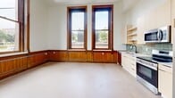 Located at 215 N First Ave E in downtown Duluth, Minnesota, this one-bedroom, one-bathroom unit offers an efficient and thoughtfully laid out single-floor plan. The space artfully combines historic architectural character with contemporary finishes throughout.

The open kitchen and living area serves as the heart of the unit, immediately drawing attention with its soaring ceilings and tall, wood-trimmed windows that flood the space with abundant natural light and views of the surrounding neighborhood. The kitchen is outfitted with light wood cabinetry, open shelving, a green subway tile backsplash, and a full suite of stainless steel appliances, including a refrigerator, electric range, microwave, and dishwasher.

Rich, warm wood wainscoting lines the lower walls of the living and bedroom areas, a nod to the building's historic heritage. The bedroom is a comfortable, well-proportioned room featuring the same large windows and classic wood detailing. A dedicated closet provides practical storage.

The bathroom includes a full tub-and-shower combination with white subway tile surround and matte black fixtures, paired with a toilet and vanity. Additional convenience is provided by an in-unit laundry area. A hallway connects the rooms, contributing to a logical and functional flow throughout this charming Duluth residence.