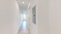 This 1-bedroom, 1-bathroom unit in Everett, MA offers a clean, modern interior designed with simplicity and functionality in mind. The single-floor layout is organized efficiently, with a spacious living area, two hallway passages, and a full bathroom.

The living area is bright and airy, bathed in natural light streaming through multiple double-hung windows that frame views of surrounding greenery. Light-toned hardwood flooring runs throughout, complementing the crisp white walls and creating a warm, contemporary atmosphere. Recessed lighting adds to the well-lit feel of the space.

The bedroom area benefits from large windows on two walls, allowing sunlight to pour in from multiple angles. A wall-mounted mini-split HVAC unit ensures year-round climate comfort. The clean, neutral palette throughout provides a versatile canvas for any style of furnishing.

The bathroom is finished to a high standard, featuring a frameless glass-enclosed walk-in shower with white tile surround, brushed nickel hardware, and a sleek, modern door. White flooring and walls carry the bright, cohesive aesthetic from the rest of the unit into this space seamlessly.

Overall, this unit presents a thoughtfully designed, move-in-ready space with modern finishes, abundant natural light, and a clean architectural aesthetic suited for comfortable everyday living in Everett, MA.