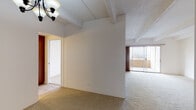 This single-floor unit is defined by a distinctive textured ceiling with exposed structural beams running throughout, lending architectural character to each room. The open living area is generously proportioned, finished with neutral wall-to-wall carpeting that extends through the main living spaces, and is anchored by a ceiling-mounted light fixture. Sliding glass doors lead directly to a balcony, offering elevated city views and filling the space with natural light.

The kitchen is thoughtfully laid out with dark wood cabinetry lining the walls, a stainless steel refrigerator, an electric range, and a single-basin sink beneath pendant lighting. A pass-through opening connects the kitchen to the living area, enhancing the sense of openness. Tile flooring runs through the kitchen and into the bathroom areas.

The bedroom features carpeted floors, a large window with city views, and a wide sliding-door closet providing ample storage. The bathroom corridor includes a dark wood vanity with a granite countertop, a vessel-style sink, decorative pendant lighting, and tile flooring. An adjacent walk-in closet adds further practicality to the space. Overall, the unit presents a functional and open layout with elevated views throughout.