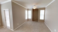 This single-floor residence offers a well-organized layout with functional living spaces throughout. The open living and dining areas are finished with neutral-toned carpet and warm beige walls, complemented by crown molding and ceiling fans with light fixtures. Multiple windows allow natural light to fill these spaces, creating a bright and comfortable atmosphere.

The kitchen is designed for practicality, featuring warm oak cabinetry, dark laminate countertops, and a full suite of black appliances, including an electric range, over-the-range microwave, dishwasher, and refrigerator. Light tile flooring and a stainless steel sink complete the functional workspace. A peninsula with a raised countertop connects the kitchen to the living area, providing both a visual boundary and additional counter space.

The primary bedroom is generously sized, with plush carpet, a ceiling fan, and direct access to an en-suite bathroom. The bathroom includes a wide vanity with dark granite-style countertops, rich wood cabinetry, a large mirror, tile flooring, and a full soaking tub with a tiled surround accented by a black tile border. Additional bedrooms are well-proportioned, each with carpet and ceiling fans, offering comfortable and versatile spaces.