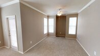 This single-floor residence offers a well-organized layout with functional living spaces throughout. The open living and dining areas are finished with neutral-toned carpet and warm beige walls, complemented by crown molding and ceiling fans with light fixtures. Multiple windows allow natural light to fill these spaces, creating a bright and comfortable atmosphere.

The kitchen is designed for practicality, featuring warm oak cabinetry, dark laminate countertops, and a full suite of black appliances, including an electric range, over-the-range microwave, dishwasher, and refrigerator. Light tile flooring and a stainless steel sink complete the functional workspace. A peninsula with a raised countertop connects the kitchen to the living area, providing both a visual boundary and additional counter space.

The primary bedroom is generously sized, with plush carpet, a ceiling fan, and direct access to an en-suite bathroom. The bathroom includes a wide vanity with dark granite-style countertops, rich wood cabinetry, a large mirror, tile flooring, and a full soaking tub with a tiled surround accented by a black tile border. Additional bedrooms are well-proportioned, each with carpet and ceiling fans, offering comfortable and versatile spaces.