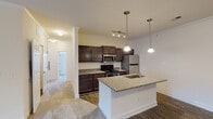 This single-story residence is thoughtfully designed with a clean, contemporary aesthetic that balances functionality and comfort throughout. The open-concept kitchen serves as a central highlight, featuring dark espresso cabinetry paired with granite countertops and a generously sized island with a built-in sink. Stainless steel appliances, including a refrigerator, range, and microwave, complement the space, while dual pendant lights and a track lighting fixture provide focused illumination. Hardwood-style flooring anchors the kitchen and adjacent living area, which is finished with crown molding and neutral walls that create a bright, welcoming atmosphere.

The living area transitions seamlessly from the kitchen and benefits from natural light, with a view toward an entry door. Bedrooms are carpeted and well-proportioned, with vaulted ceilings adding an airy quality to the primary suite. The primary bedroom includes direct access to a walk-in closet and an en-suite bathroom featuring dark cabinetry, granite countertops, hardwood-style flooring, and a walk-in shower with chrome fixtures. A secondary bedroom offers a large window with outdoor tree views, filling the room with natural light. The additional bathroom echoes the same finishes, maintaining design consistency throughout the home.