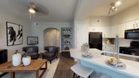 Located at 1000 Fanfare Way in Alpharetta, GA, this single-story residence offers a thoughtfully designed open-concept layout with elegant architectural details and quality finishes throughout. A graceful arched entryway introduces the main living area, where rich dark hardwood-style flooring, neutral tones, and abundant natural light from large windows create a warm and inviting atmosphere. The living room provides generous space for seating, complemented by ceiling fans and framed wall art that add character to the space. The kitchen is a standout feature, boasting white cabinetry, quartz countertops, a large peninsula with bar seating, a deep undermount sink, and black appliances. Built-in shelving near the entryway adds both function and style. The dining area accommodates a full-sized table and bench seating, with floor-to-ceiling draping and ample window light. The primary bedroom is carpeted and serene, with large windows and access to a well-appointed en-suite bathroom featuring quartz vanity countertops, a walk-in shower, a soaking tub, and a spacious walk-in closet. Additional bedrooms offer comfortable carpet flooring, natural light, and closet access. A secondary bathroom includes a tiled tub-shower combination and hardwood-style flooring, completing this refined and functional home.