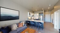 This thoughtfully designed single-floor residence offers a seamless blend of modern aesthetics and functional living. The open-concept layout connects the kitchen and living area, creating an inviting and cohesive space ideal for both everyday living and entertaining.

The kitchen is a standout feature, showcasing a two-tone cabinetry scheme with dark lower cabinets and crisp white upper cabinets, complemented by a subway tile backsplash and quartz countertops. A large island with bar seating and pendant lighting serves as the centerpiece, while stainless steel appliances — including a French door refrigerator, range, microwave, and dishwasher — complete the well-equipped space.

The living area is bathed in natural light through large windows dressed with blinds and sheer curtains, offering views of the surrounding greenery. Light wood-style flooring runs throughout the main areas, adding warmth and continuity to the space.

The bedroom is a calm retreat, featuring large windows that invite natural light, plush carpeting, and wall-mounted shelving for display. The bathroom offers a clean, modern design with wood-tone cabinetry, a glass-enclosed walk-in shower, and durable wood-style flooring. The entry hallway includes closet storage, providing practical organization from the moment you step inside.