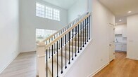 Located at 275 Dorset Ave in Oswego, Illinois, this two-story home is designed with clean, modern finishes throughout. The main level immediately impresses with soaring two-story ceilings in the living area, flooding the space with natural light through large windows. Light wood-tone laminate flooring extends across the main level, complementing the bright, white walls and open layout. The staircase serves as a striking architectural feature, showcasing a wood handrail paired with sleek black metal balusters and carpeted treads, overlooked by an upper-level balcony railing of matching design.

The kitchen is outfitted with white cabinetry, light countertops, and stainless steel appliances, including a gas range and over-the-range microwave. Upstairs, the bedrooms are finished with plush carpeting, neutral gray walls, ceiling fans, and ample natural light. A generously sized walk-in closet features wire shelving for organized storage. The bathrooms include a tiled walk-in shower with a glass door and chrome fixtures, as well as a full tub-shower combination with clean white surround. A dedicated laundry room on the upper level provides added convenience, complete with a washer and dryer and easy-care wood-look flooring.