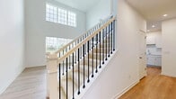 Located at 275 Dorset Ave in Oswego, Illinois, this two-story home is designed with clean, modern finishes throughout. The main level immediately impresses with soaring two-story ceilings in the living area, flooding the space with natural light through large windows. Light wood-tone laminate flooring extends across the main level, complementing the bright, white walls and open layout. The staircase serves as a striking architectural feature, showcasing a wood handrail paired with sleek black metal balusters and carpeted treads, overlooked by an upper-level balcony railing of matching design.

The kitchen is outfitted with white cabinetry, light countertops, and stainless steel appliances, including a gas range and over-the-range microwave. Upstairs, the bedrooms are finished with plush carpeting, neutral gray walls, ceiling fans, and ample natural light. A generously sized walk-in closet features wire shelving for organized storage. The bathrooms include a tiled walk-in shower with a glass door and chrome fixtures, as well as a full tub-shower combination with clean white surround. A dedicated laundry room on the upper level provides added convenience, complete with a washer and dryer and easy-care wood-look flooring.