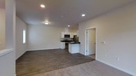 This single-floor space offers a clean, modern design with an open-concept layout that seamlessly connects the living, dining, and kitchen areas. The kitchen is well-appointed with white cabinetry, dark countertops, and a full suite of stainless steel appliances, including a range, microwave, and refrigerator. A peninsula-style counter provides additional workspace and serves as a natural divider between the kitchen and the open living area. Recessed lighting throughout the space ensures consistent, well-distributed illumination, complemented by flush-mount ceiling fixtures. The flooring transitions from durable hardwood-style planks in the kitchen and main areas to plush carpeting in the living space, adding warmth and comfort underfoot. Neutral, light-toned walls create a bright and airy ambiance, making the space feel open and inviting. A doorway visible from the main area leads to additional rooms, suggesting a functional and well-organized floor plan. The overall design aesthetic is contemporary and minimalist, with clean lines and a neutral color palette that provides a versatile backdrop for a variety of interior styles.