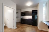 Located at 3635 Phinney Ave N in Seattle's vibrant Phinney Ridge neighborhood, this studio unit offers a thoughtfully designed single-floor layout that maximizes every square foot. The open-plan living, dining, and kitchen area forms the heart of the space, centered around a sleek kitchenette finished in dark espresso cabinetry with silver hardware. The kitchen is equipped with a full-size black refrigerator, over-the-range microwave, single-basin sink with a chrome faucet, and light-colored countertops that contrast cleanly against the dark cabinetry. A built-in bench with integrated hooks sits beneath a window that frames views of surrounding greenery, providing natural light and a functional entryway nook. The living area is bright and open, featuring neutral white walls and warm wood-look flooring that runs throughout the entire unit, lending a cohesive and modern aesthetic. A baseboard heater ensures year-round comfort. Wall-mounted hooks near the entry provide practical storage. The private bathroom, accessible through a dedicated doorway, completes the layout. Clean lines, a neutral color palette, and contemporary finishes give this unit a modern, move-in-ready feel suited for efficient urban living.