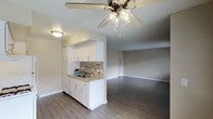 This single-floor space offers a well-designed, open-concept layout that seamlessly connects the kitchenette to the living area, creating a sense of openness and ease of movement throughout. The kitchenette is outfitted with crisp white cabinetry, a stainless steel sink, and a tasteful tile backsplash in a mosaic pattern that adds a touch of visual interest. Light-toned countertops complement the cabinetry, while the inclusion of a refrigerator ensures full functionality in a compact footprint. The kitchen area transitions naturally into the generously sized living space, which is distinguished by warm, hardwood-style plank flooring that runs consistently throughout the unit, lending a cohesive and inviting feel. Neutral-toned walls provide a versatile backdrop, allowing for a variety of décor styles. A ceiling fan with an integrated light fixture serves as a central element of the main living area, offering both comfort and illumination. Recessed and flush-mount lighting provide additional brightness, contributing to the overall welcoming ambiance. Clean baseboards and smooth wall transitions reflect careful attention to detail throughout the space, making it a practical and comfortable environment.