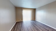 This single-floor unit presents a well-organized layout that balances open communal areas with more private rooms. The main living area is finished with durable wood-look plank flooring in a warm grey-brown tone, complemented by neutral taupe walls and clean white baseboards. A large sliding glass door fitted with vertical blinds serves as a prominent feature, allowing natural light to fill the space while offering access to the outdoors.

The kitchen is positioned adjacent to the living area and is separated by a half-wall peninsula with a granite countertop, creating an open, connected feel. The kitchen itself is equipped with white cabinetry featuring contemporary hardware, granite countertops with a double stainless steel sink, a black refrigerator, and a dishwasher. The same wood-look flooring extends throughout this area, maintaining visual continuity.

The bedrooms are carpeted in a neutral beige tone and feature ceiling fans, providing comfort and climate control. One bedroom includes a built-in shelving closet, offering practical storage. The rooms are painted in soft grey-blue tones, lending a calm, cohesive atmosphere throughout. Overall, the unit presents a clean, functional, and move-in ready environment.