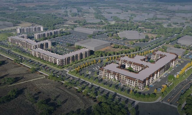 Elevated aerial view of Sageland Flats at Brooks showing residential buildings, parking lots, tree lined streets, and nearby open land - Sageland Flats at Brooks