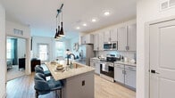 Located at 4535 SW 54th St Rd in Ocala, Florida, this single-story, one-bedroom, one-bathroom residence offers a thoughtfully designed layout that maximizes every square foot. The open-concept living and kitchen area is the heart of the home, where light-toned luxury vinyl plank flooring flows seamlessly throughout. The kitchen is outfitted with gray shaker-style cabinetry, light granite countertops, a full suite of stainless steel appliances, a subway tile backsplash, and a central island with an undermount sink and seating — finished with striking pendant lighting overhead. The living room is bright and airy, with large windows allowing abundant natural light and a ceiling fan overhead. The bedroom is a comfortable retreat featuring plush carpeting, a ceiling fan, and a window with outdoor views. It connects directly to a walk-in closet with multi-tier wire shelving and to the full bathroom, which features a dual-sink granite vanity, wood-toned cabinetry, wood-look flooring, and a soaking tub with tile surround. Additional functional spaces include a dedicated laundry area, pantry, and utility room, ensuring ample storage and convenience throughout this efficiently planned residence.