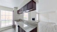This single-story residence offers a well-organized layout that balances functional living spaces with modern finishes throughout. The kitchen is a standout feature, equipped with dark espresso-toned cabinetry, granite countertops with subtle grey veining, a stainless steel sink, and stainless steel appliances including a full-size refrigerator. Upper cabinets suspended above the peninsula provide additional storage while maintaining an open sightline into the living area. Natural light filters through multiple windows fitted with horizontal blinds, brightening both the kitchen and adjoining spaces.

The living room is generously proportioned, featuring light-toned hardwood-style flooring, neutral grey walls, and a centrally positioned fireplace that serves as a natural focal point. Multiple windows allow ample daylight into the space, creating a bright and welcoming atmosphere.

The bedrooms are finished with plush carpeting and ceiling fans, offering a comfortable and quiet retreat. Closet space is provided, and windows ensure each room receives natural light. The bathrooms each feature a full tub and shower combination with clean white tile surrounds and chrome fixtures, maintaining a simple and functional aesthetic throughout.