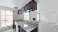 This single-story residence offers a well-organized layout that balances functional living spaces with modern finishes throughout. The kitchen is a standout feature, equipped with dark espresso-toned cabinetry, granite countertops with subtle grey veining, a stainless steel sink, and stainless steel appliances including a full-size refrigerator. Upper cabinets suspended above the peninsula provide additional storage while maintaining an open sightline into the living area. Natural light filters through multiple windows fitted with horizontal blinds, brightening both the kitchen and adjoining spaces.

The living room is generously proportioned, featuring light-toned hardwood-style flooring, neutral grey walls, and a centrally positioned fireplace that serves as a natural focal point. Multiple windows allow ample daylight into the space, creating a bright and welcoming atmosphere.

The bedrooms are finished with plush carpeting and ceiling fans, offering a comfortable and quiet retreat. Closet space is provided, and windows ensure each room receives natural light. The bathrooms each feature a full tub and shower combination with clean white tile surrounds and chrome fixtures, maintaining a simple and functional aesthetic throughout.