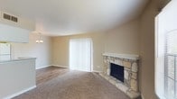 This single-story space offers a welcoming layout with clearly defined living areas and practical finishes throughout. The entry foyer features hardwood-style flooring and opens directly into the main living area, which is separated by a half-wall column that adds architectural interest while maintaining an open feel. The living room is carpeted and anchored by a standout natural stone fireplace with a white mantle, serving as a focal point of the space. Vertical blinds covering a sliding door allow for adjustable natural light. A decorative chandelier adds a subtle touch of character near the dining area.

The bedroom is carpeted and benefits from natural light through a window, complemented by a ceiling fan with a light fixture. An adjacent closet provides wire shelving for organized storage. The textured ceiling adds a classic finish consistent throughout the space.

The bathroom is efficiently designed, featuring wood-style flooring, white cabinetry above the toilet for additional storage, a vanity with a light stone countertop, and a tiled tub and shower combination. The neutral color palette maintained across all rooms contributes to a cohesive and clean overall ambiance.